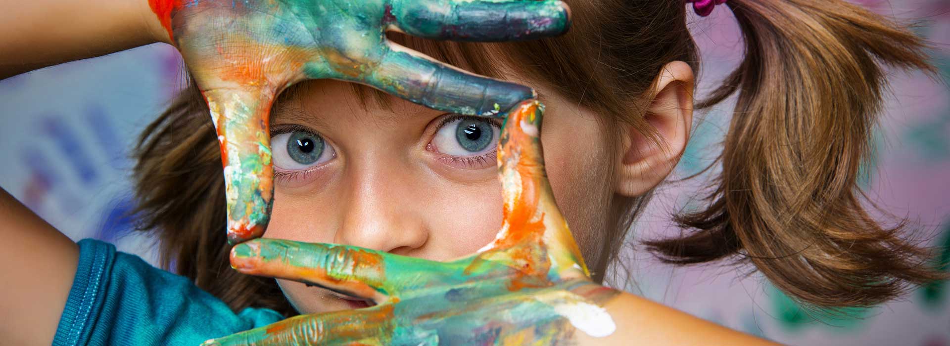 Mädchen mit farbigen Händen vor dem Gesicht